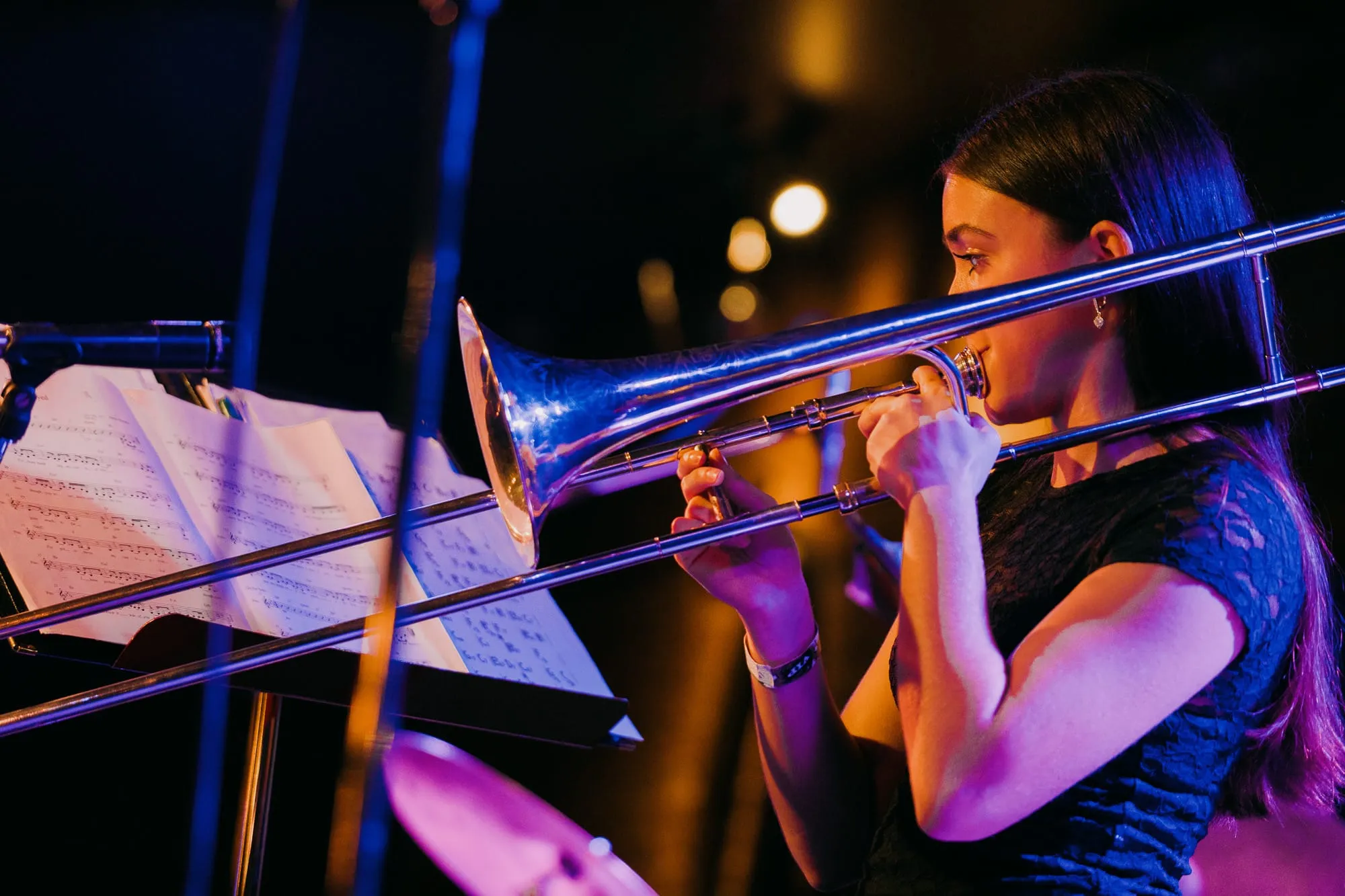 A young trombonist plays under purple stage light