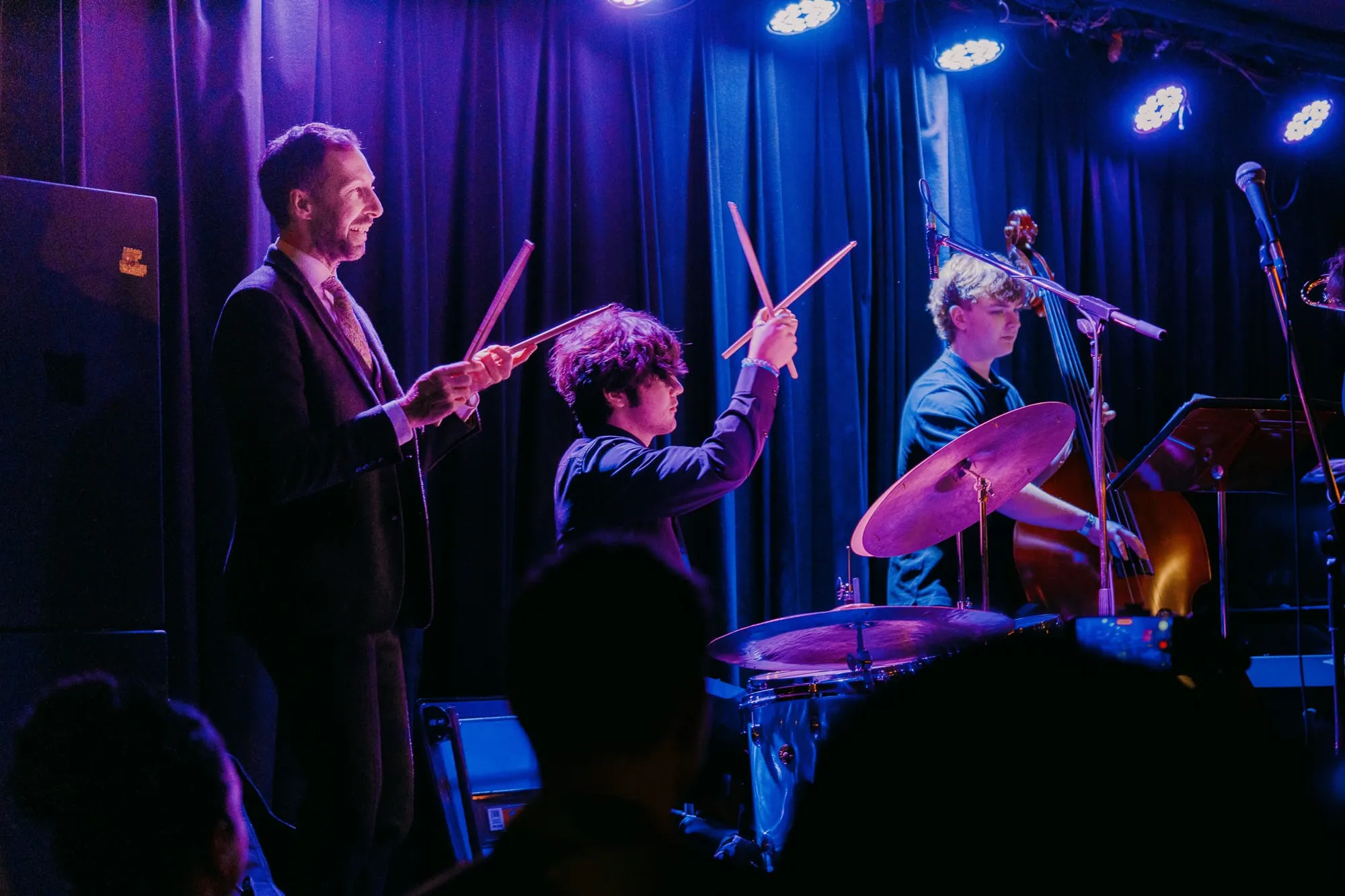 A drummer and bandmates on stage in blue light